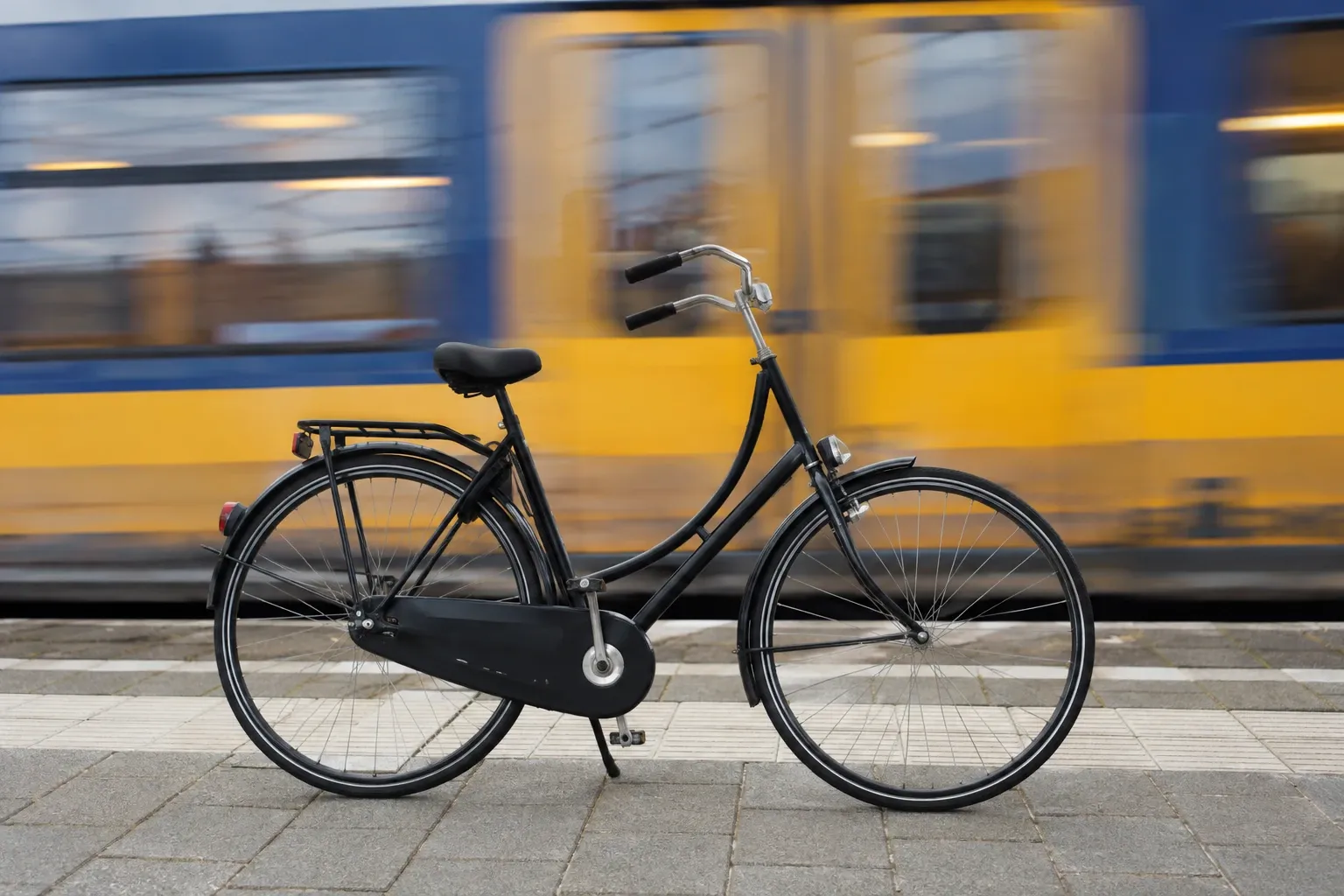Zwarte stadsfiets geparkeerd op perron met voorbijrijnde gele en blauwe trein